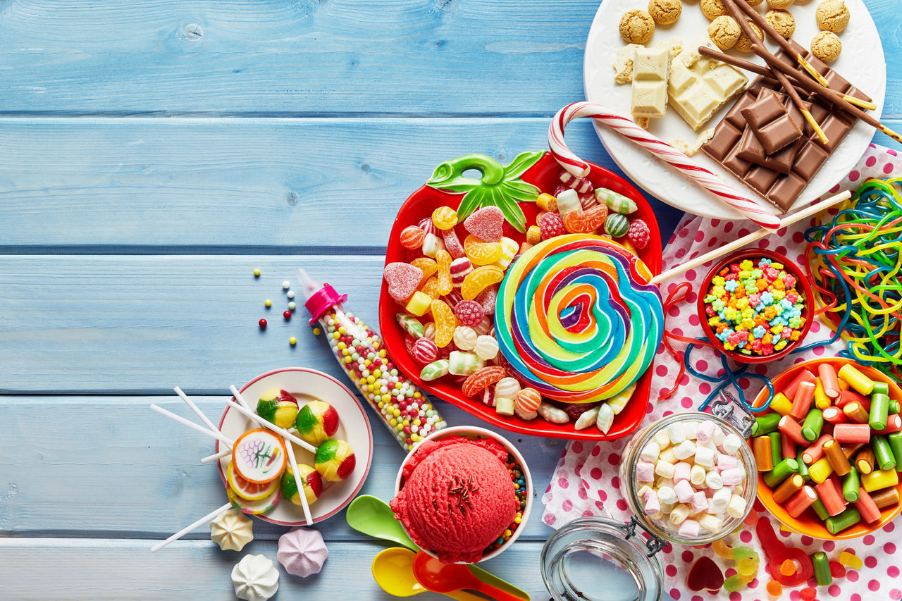 Overhead view of colorful array of different childs sweets and treats in bowls on light blue wood background; Shutterstock ID 711008224; purchase_order: CORP; job: Turkey Landing Page; client: ; other: 