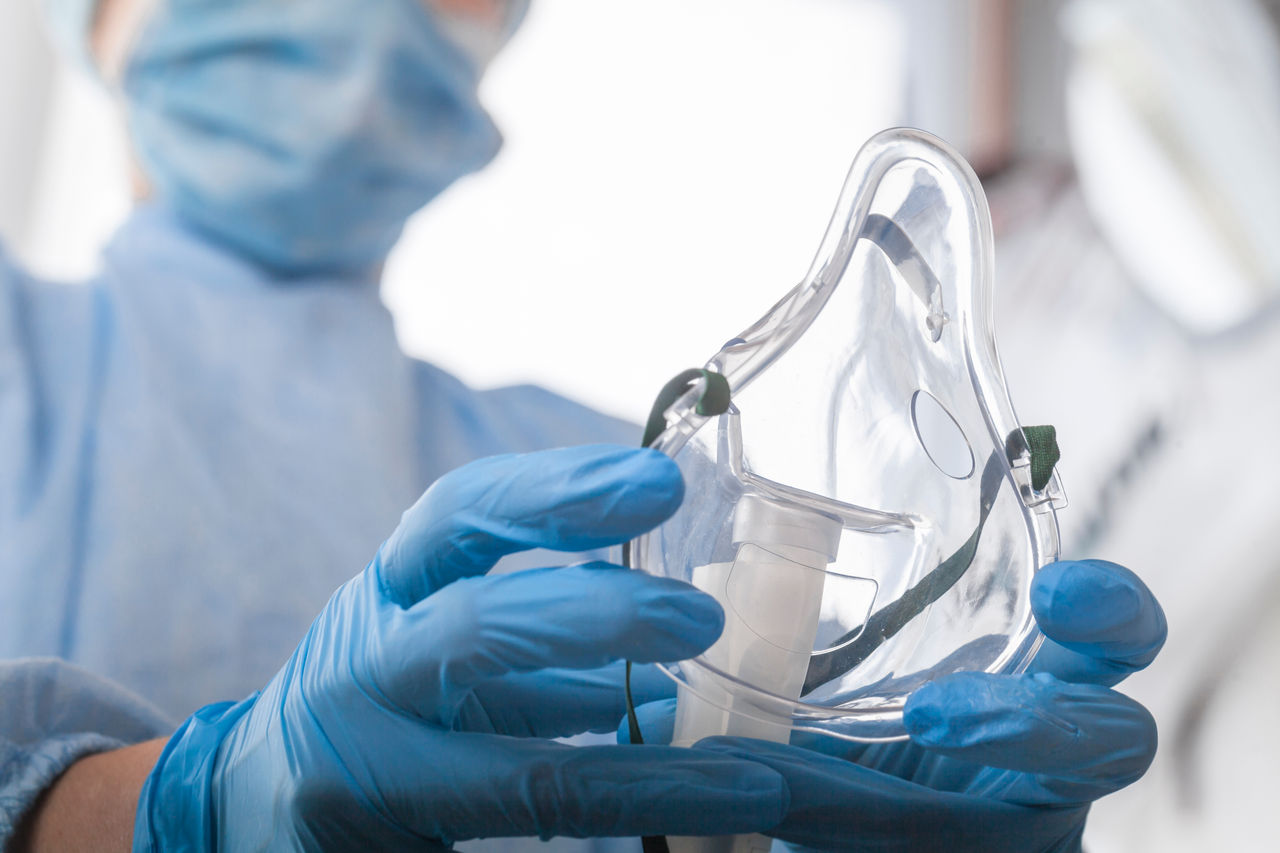 doctor in protective equipment and gloves put on oxygen mask patient diagnosis of coronavirus and Pneumonia  ; Shutterstock ID 1695703903; purchase_order: OPP Media & Collateral; job: ; client: ; other: 