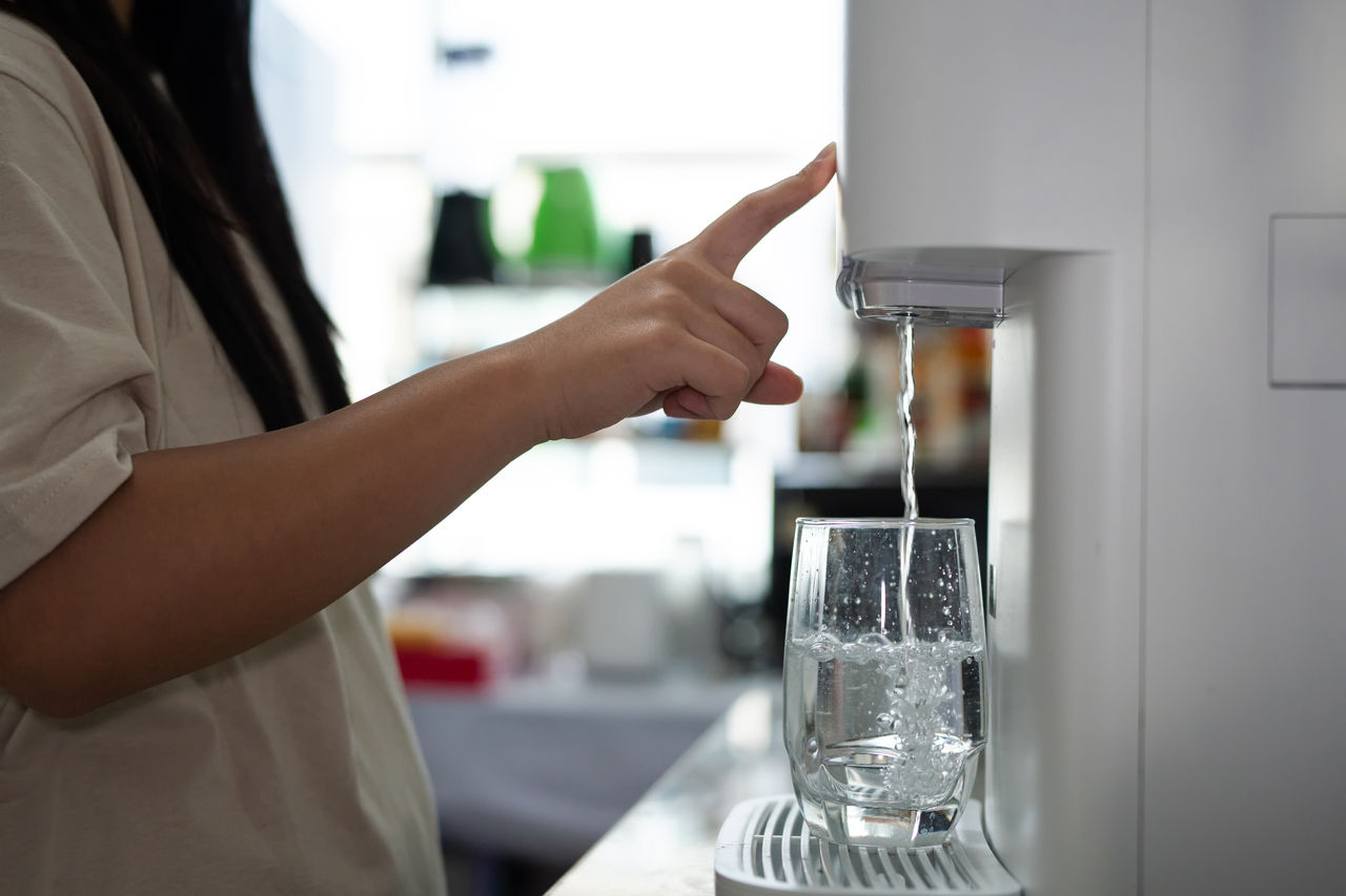Home water purifier. Modern water dispenser filling a glass; hand pressing the button for fresh water,Close up shot of a person s hand filling a glass from water purifier.; Shutterstock ID 2755724541; purchase_order: OPP Media & Collateral; job: ; client: ; other: 